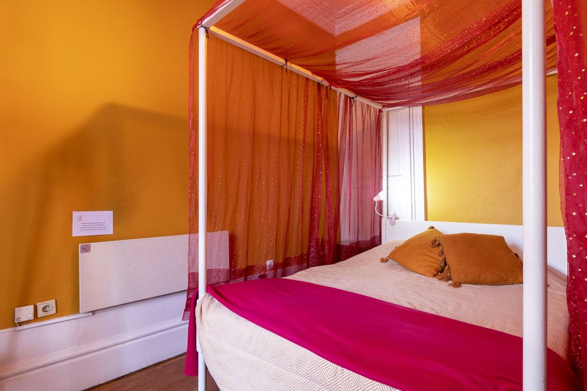 A single bed with a canopy, a bedside table, and a wall-mounted light.