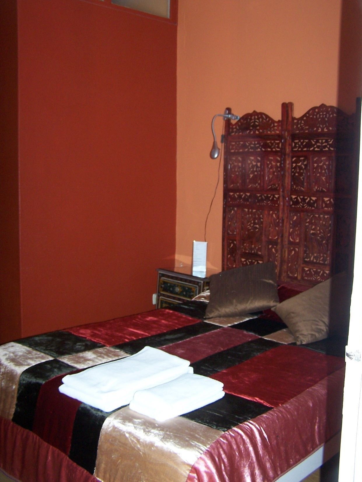 A bed with a red and black quilt, a wooden headboard, and a small bedside table with a lamp.