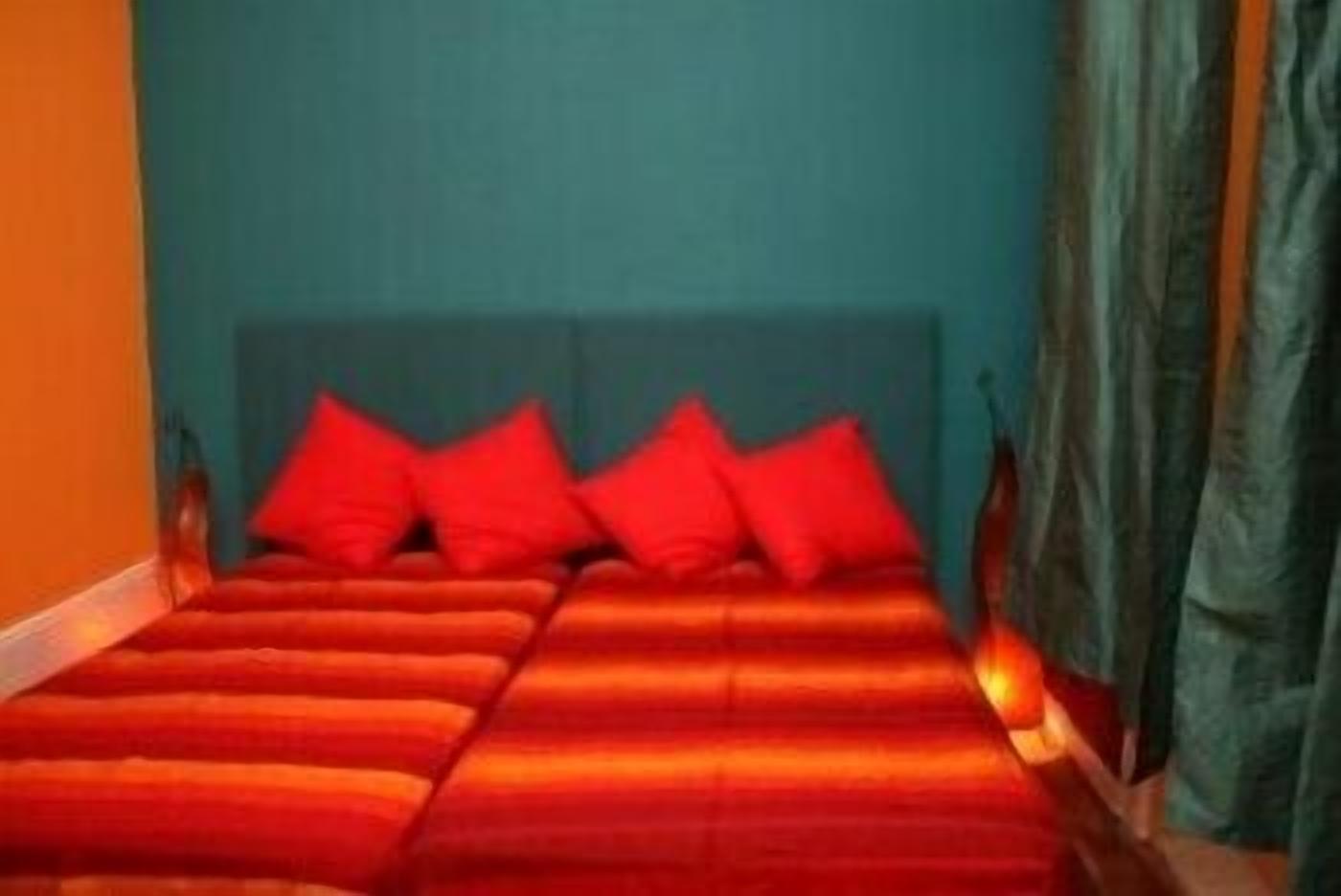 Un lit avec un cadre en bois et une literie rouge, dans une pièce aux murs de couleur turquoise et ornée d’un rideau.
