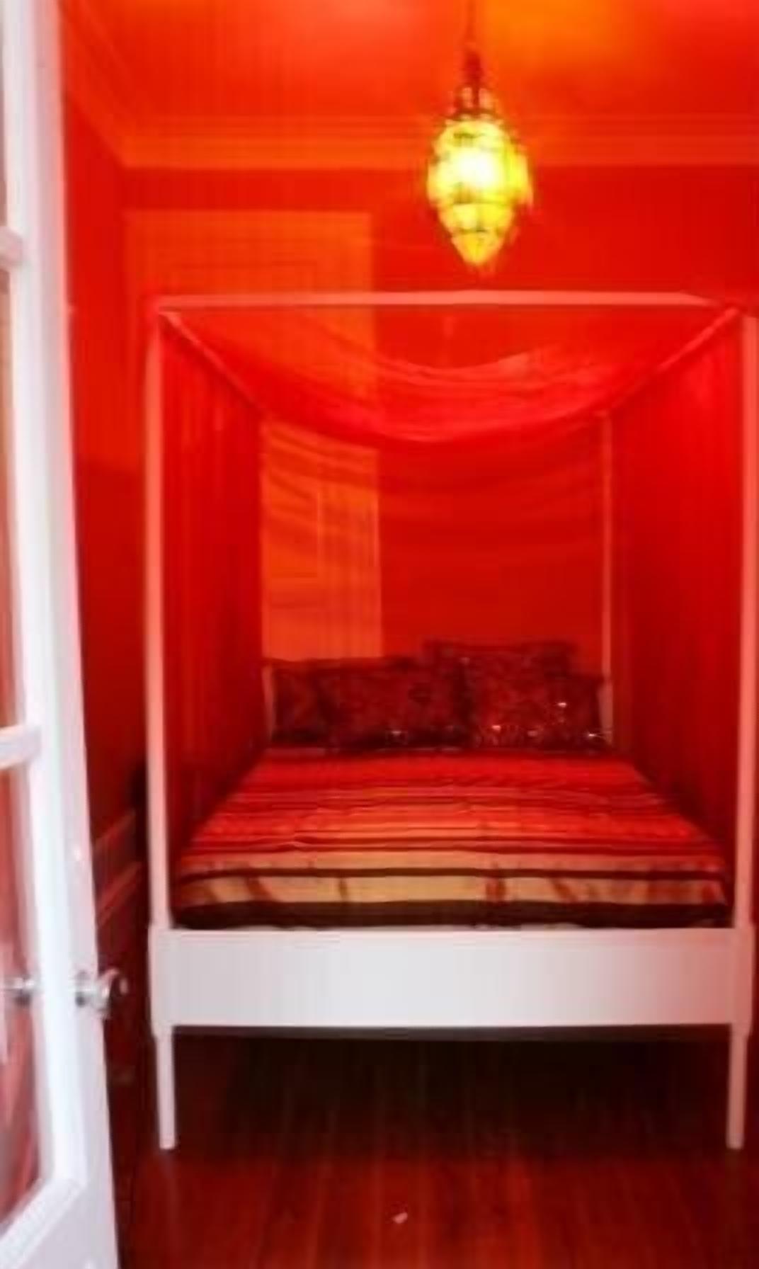 Une chambre avec un lit à baldaquin, des rideaux rouges et un luminaire suspendu.