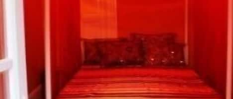 A room with a four-poster bed, red drapes, and a hanging light fixture.