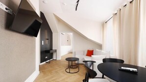 A modern loft-style room with a dining area, a sofa, and a TV mounted on the wall. - Hetman Main Square Apartments (Kraków)