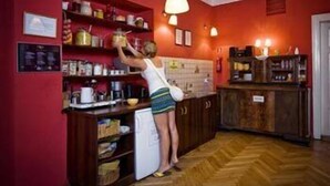 Cozinha com armários de madeira, uma geladeira e uma pessoa alcançando objetos nas prateleiras.