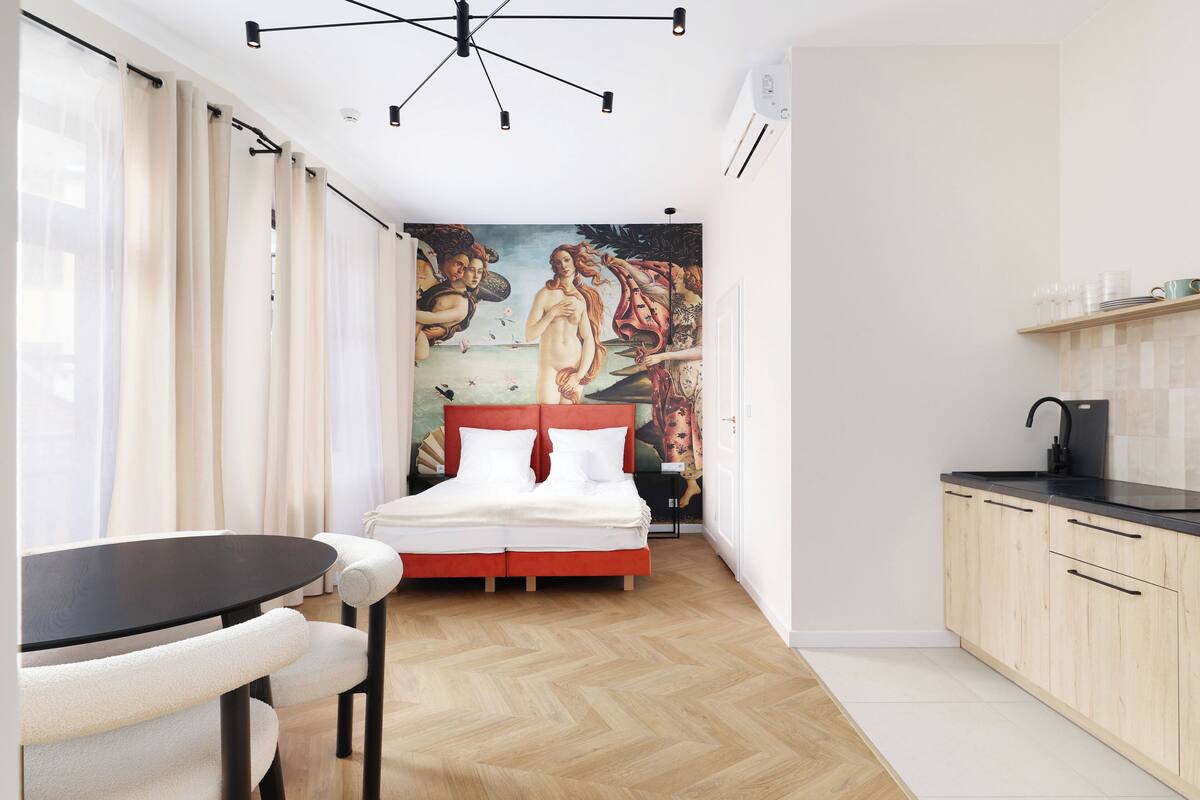 A bedroom with a bed, a dining table, and a kitchen area.