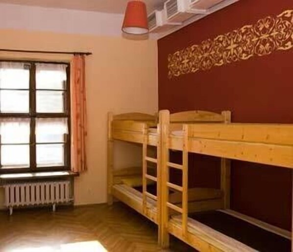 Una habitación con literas, un radiador, una ventana con cortinas y una pared decorada.