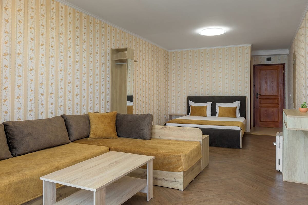 A hotel room with a sofa, a bed with two pillows, a small table, and a wooden cabinet.