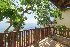 Un balcón con vista al mar, barandilla de madera y pared de piedra.