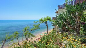 Vista de una playa con agua azul cristalina, arena dorada y un edificio con balcón con vistas al mar.