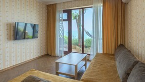 Sala de estar con sofá, una mesa y televisor. Se ve el mar a través de un ventanal.