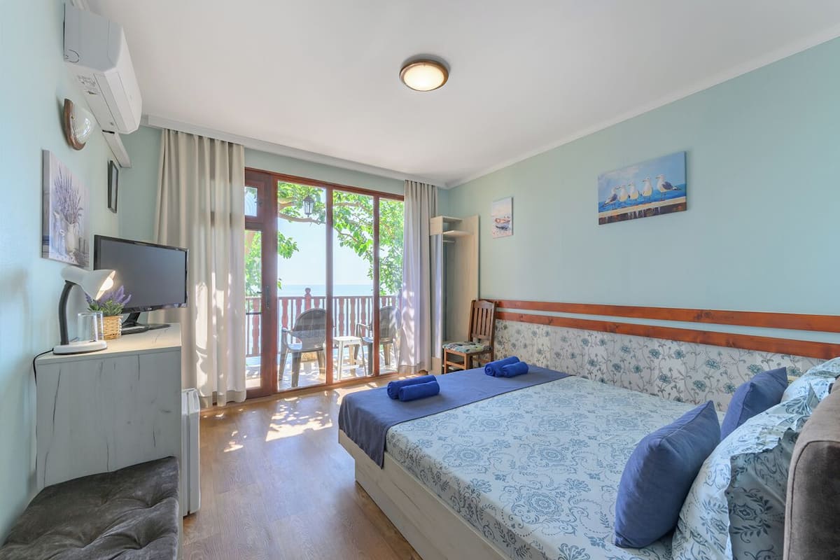 A hotel room with a bed, a desk with a computer, a TV, and a balcony with chairs.