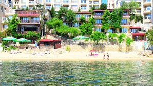 Un hotel frente a la playa con varios balcones, sombrillas y una playa de arena.