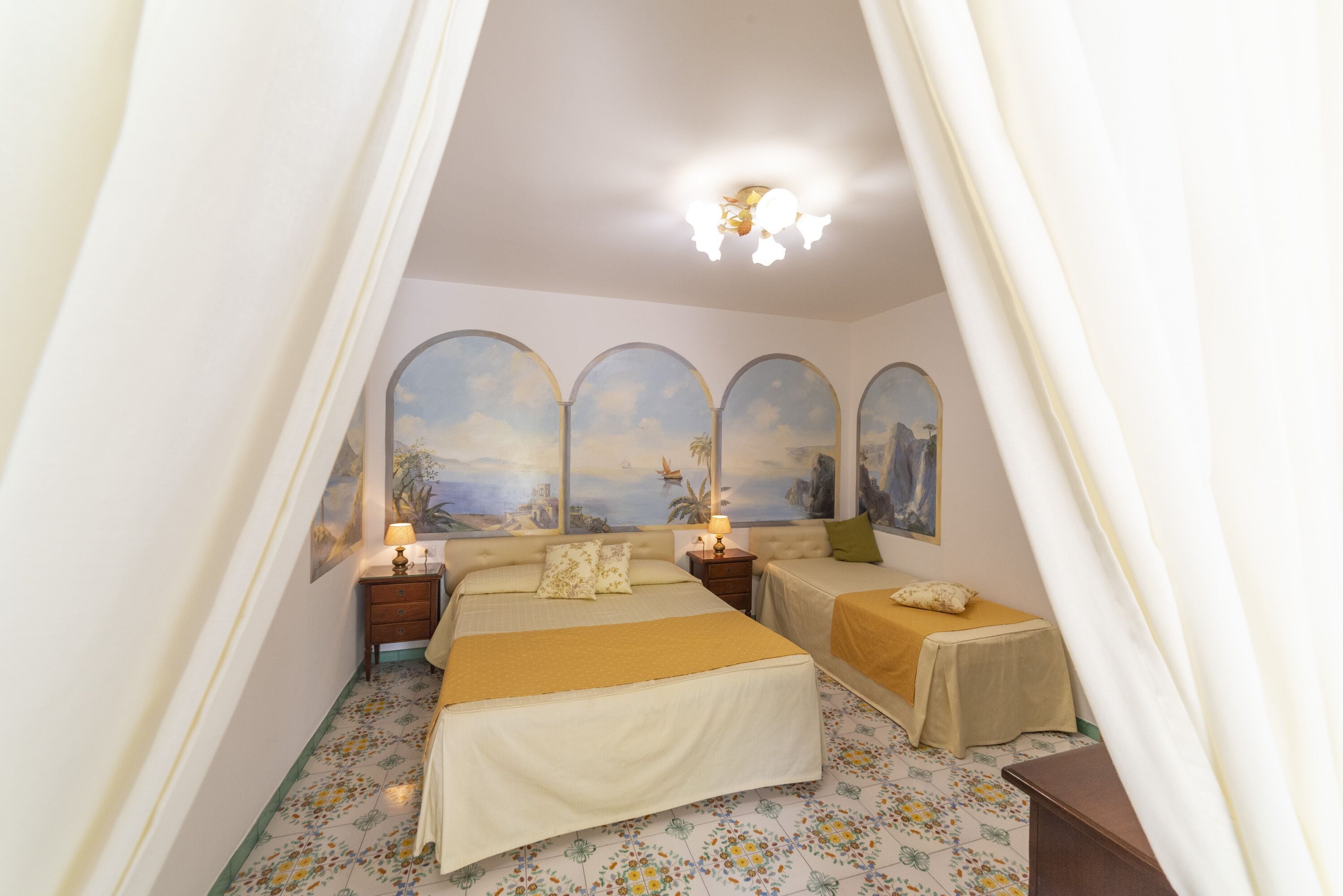 A bedroom with a large bed, two smaller beds, a nightstand with a lamp, and a ceiling light.