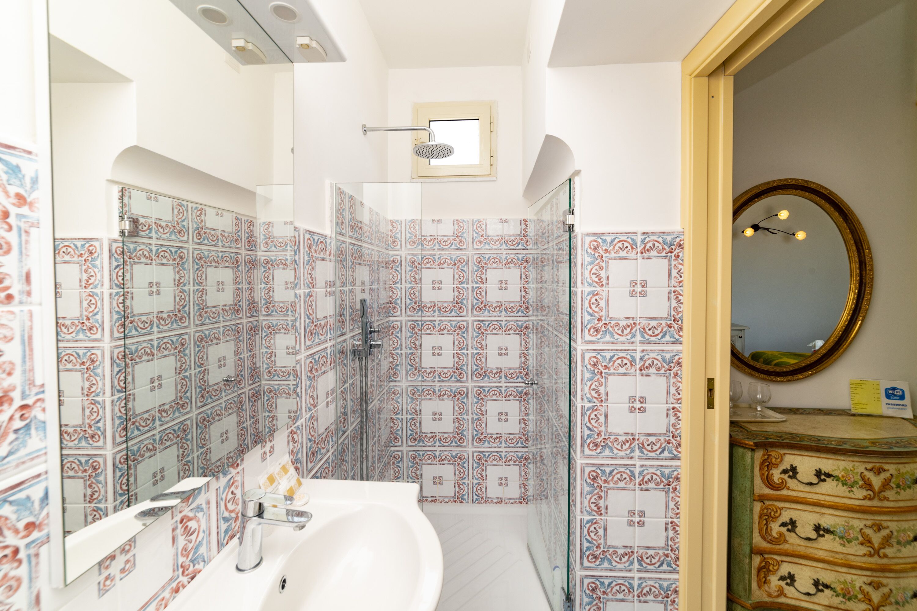 Un baño con baldosas estampadas, un lavamanos, un espejo y un mueble de tocador con cajones.