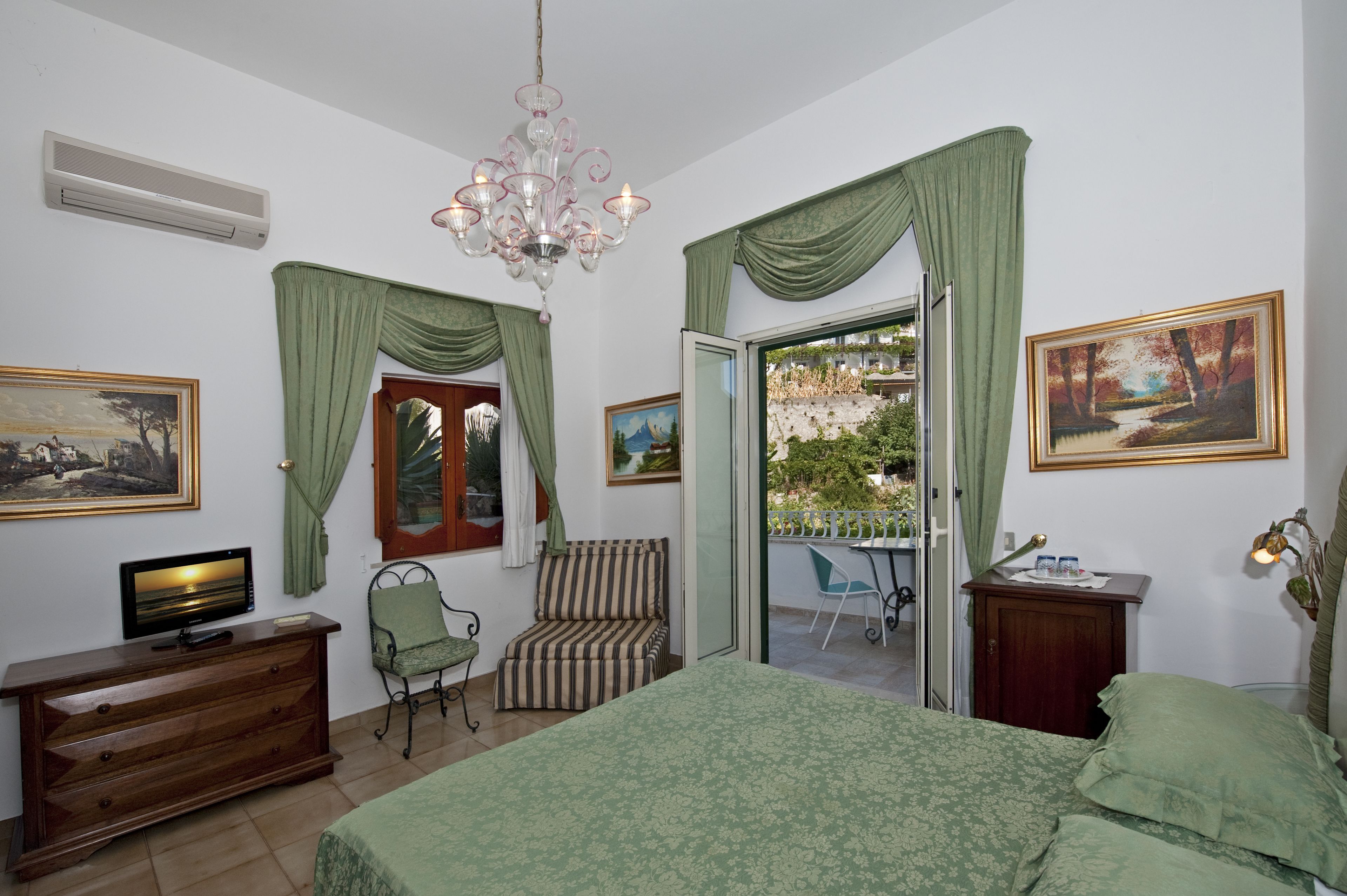 A bedroom with a bed, a TV, a chair, a desk, and a balcony with a view.