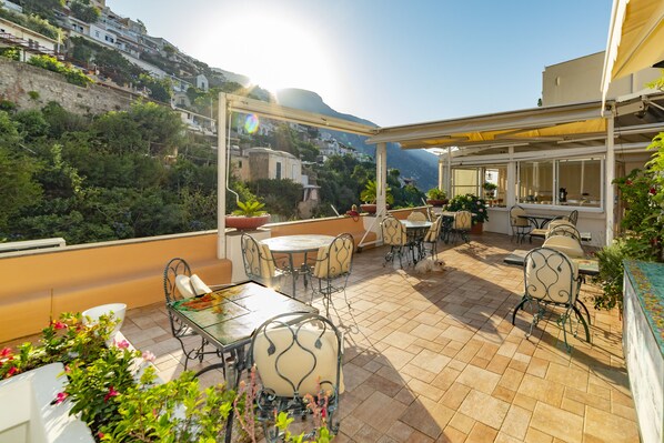 A rooftop terrace with outdoor seating, potted plants, and a view of a hillside town. - Casa Teresa (Positano)