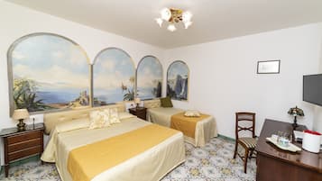 Hotelkamer met twee bedden, een bureau, een stoel, een televisie en een groot schilderij van een kustlandschap.