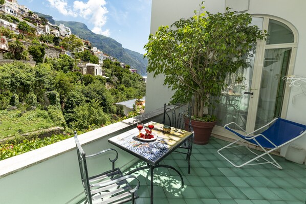 A balcony with a table set for two, a chair, and a potted plant. - Casa Teresa (Positano)