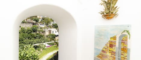 A white archway leading to a garden with a view of a hillside town.