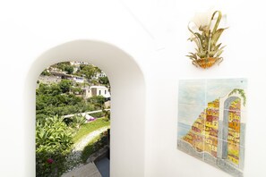 A white archway leading to a garden with a view of a hillside town. - Casa Teresa (Positano)