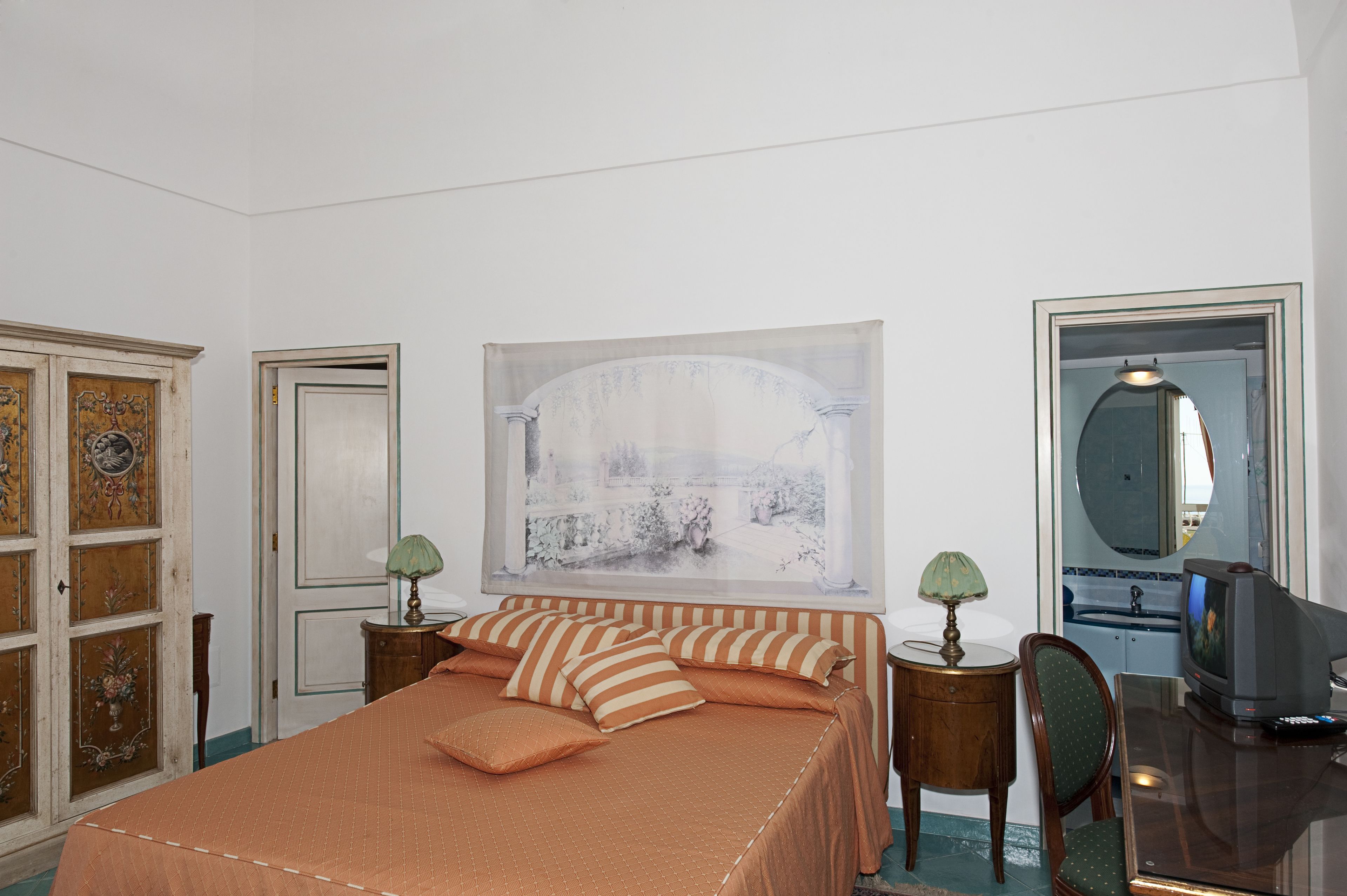 Ein Hotelzimmer mit einem großen Bett, einem Fernseher, einem Schreibtisch und einem Spiegel.