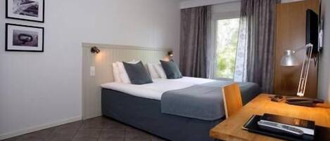 Habitación de hotel con cama, escritorio y una silla. Dos cuadros enmarcados adornan la pared.