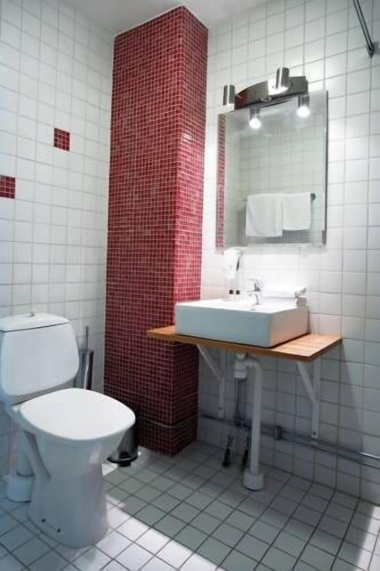A bathroom with a white toilet, a sink with a mirror above it, and a red-tiled wall.