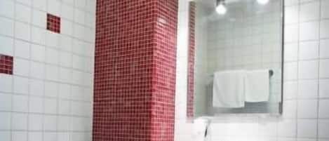 A bathroom with a white toilet, a sink with a mirror above it, and a red-tiled wall.