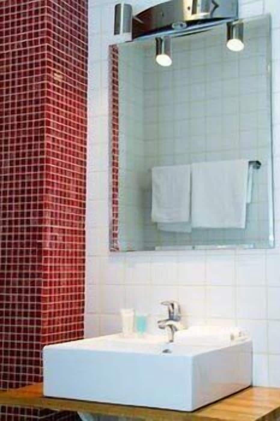 A bathroom with a white sink, a mirror, and a red-tiled wall.