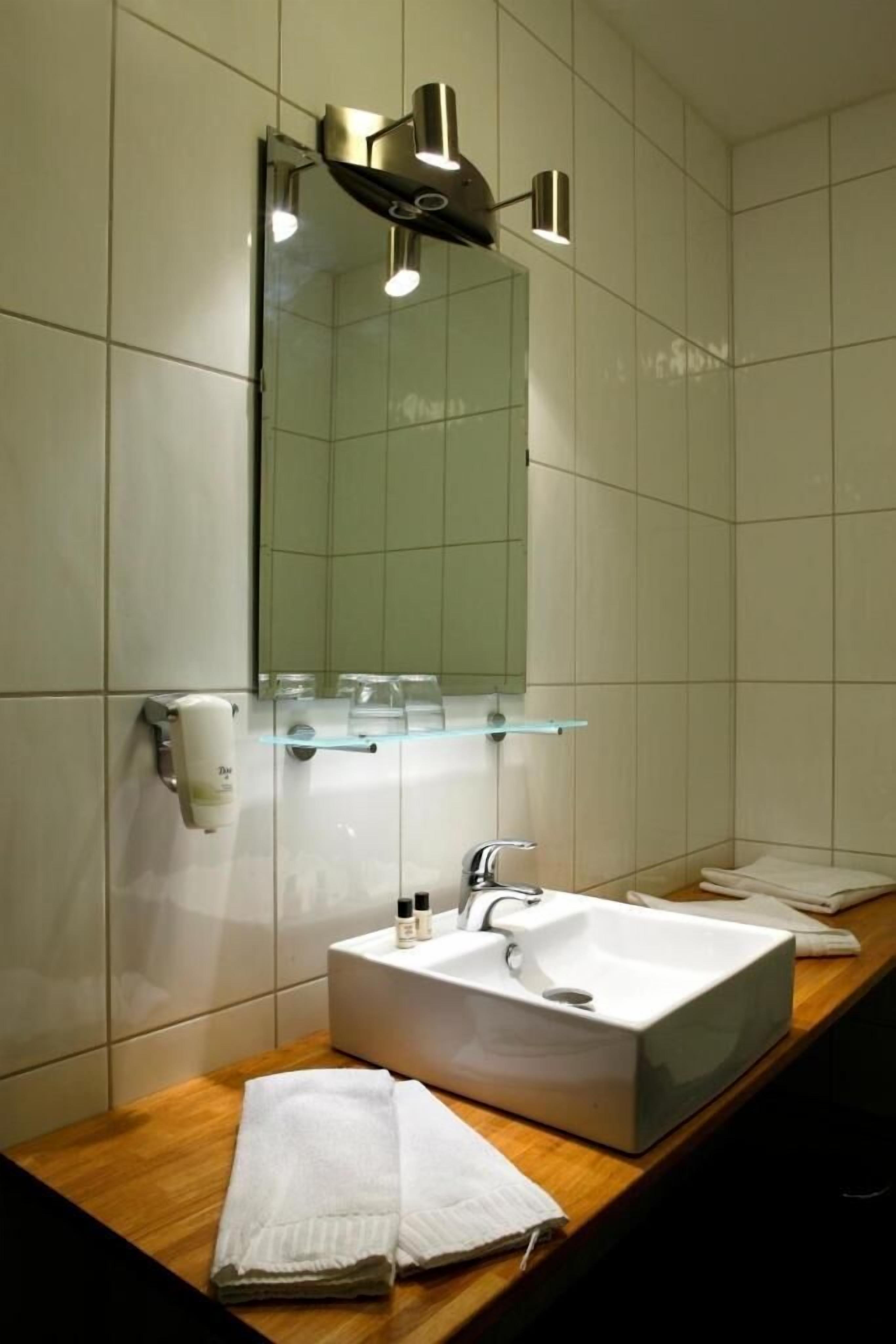 Un baño con un lavamanos blanco, un espejo y un estante de vidrio sobre el lavamanos.