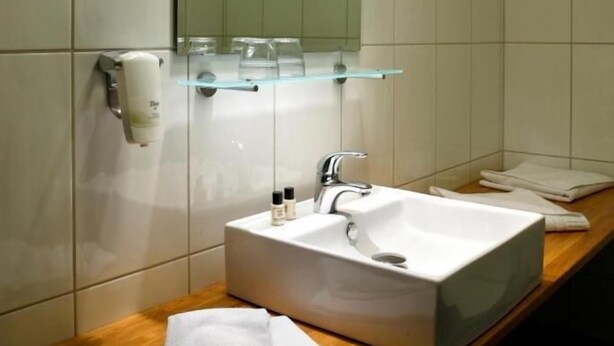Un baño con un lavamanos blanco, un espejo y un estante de vidrio sobre el lavamanos.