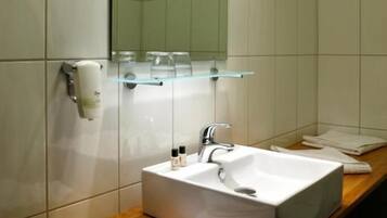 Un baño con un lavamanos blanco, un espejo y un estante de vidrio sobre el lavamanos.
