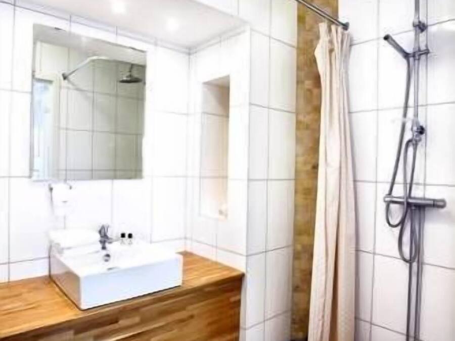 Un baño moderno con tocador de madera, un espejo grande, ducha con cortina y paredes con azulejos.