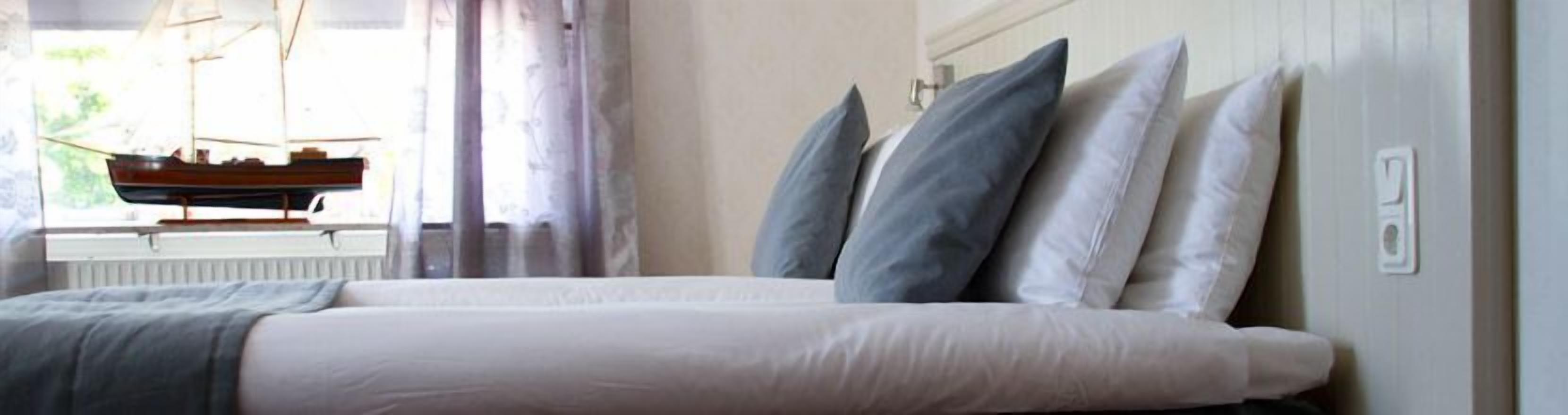 A bedroom with a bed, pillows, a radiator, and a window with curtains.