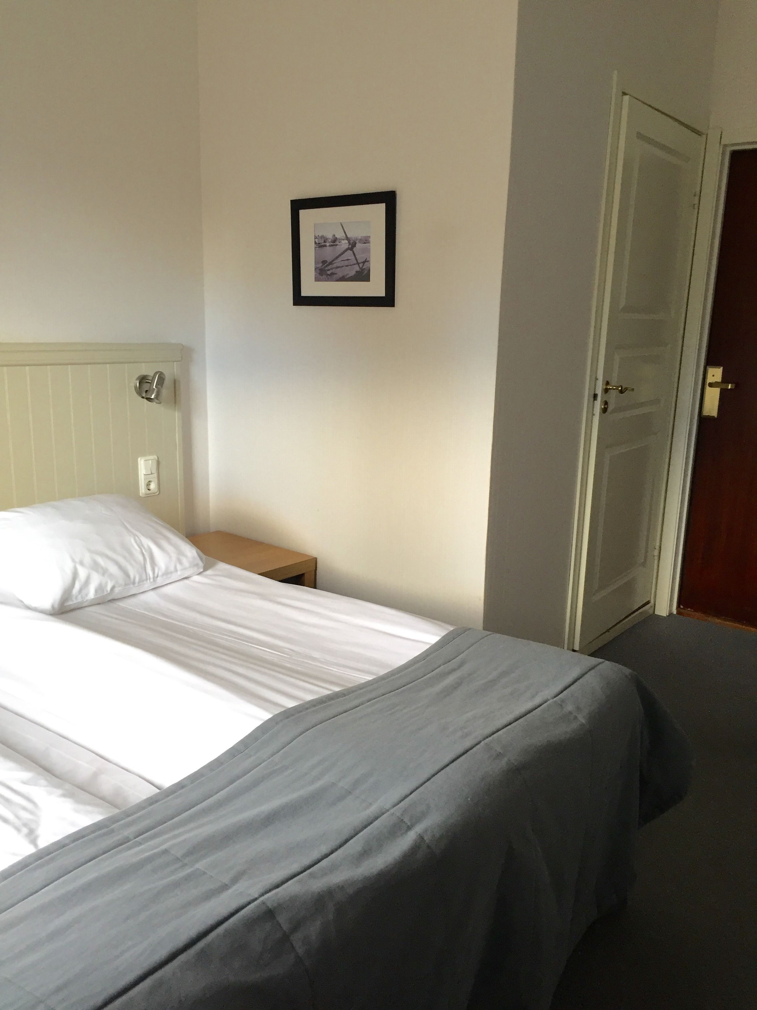 Un dormitorio con una cama, una mesita de noche, un cuadro enmarcado en la pared y una puerta.