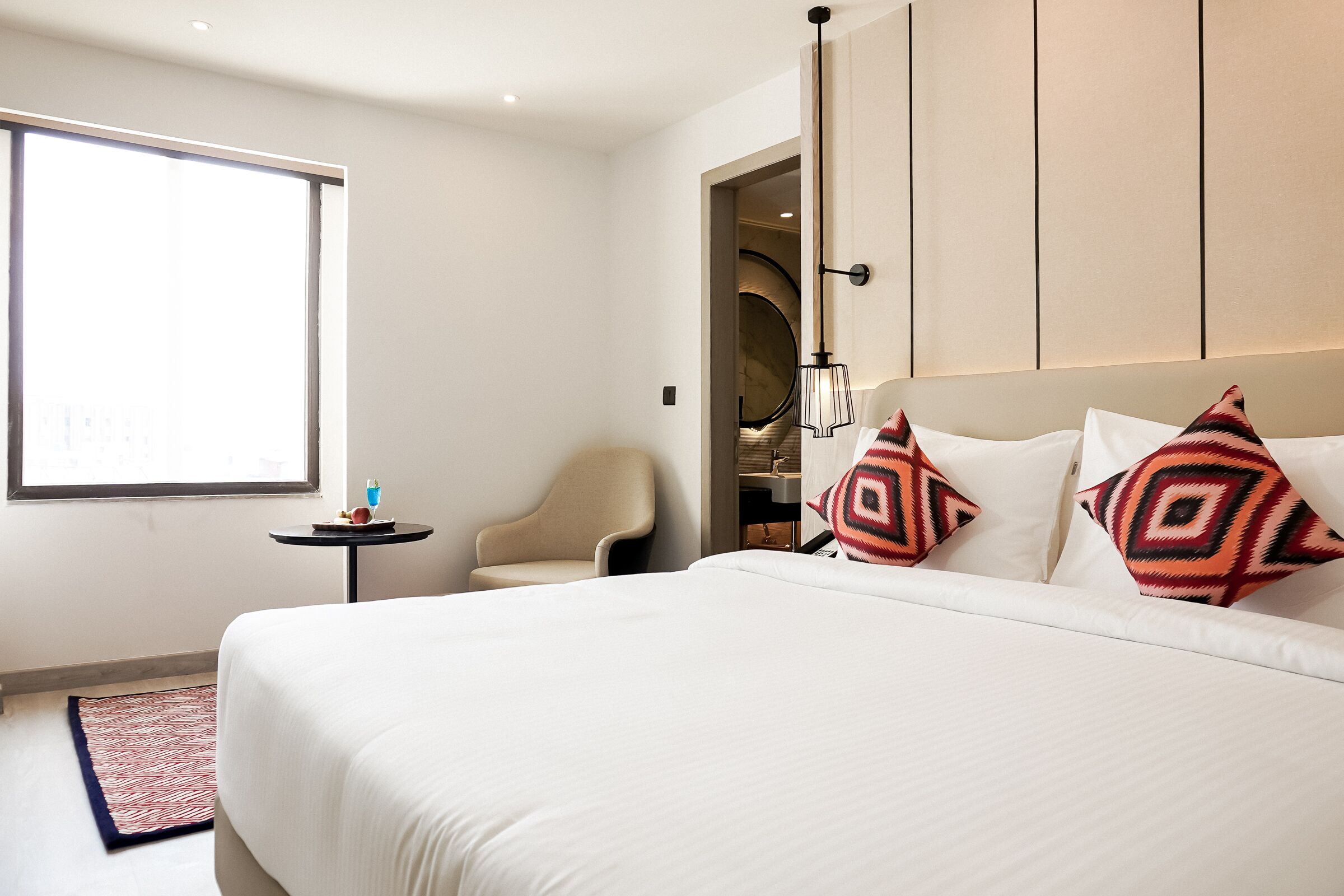 A hotel room with a large bed, a chair, a small table, and a window.