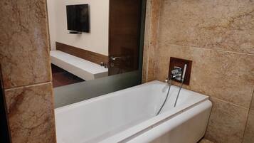 Une salle de bain moderne avec une grande baignoire, un téléviseur fixé au mur et un miroir qui reflète le meuble-lavabo.