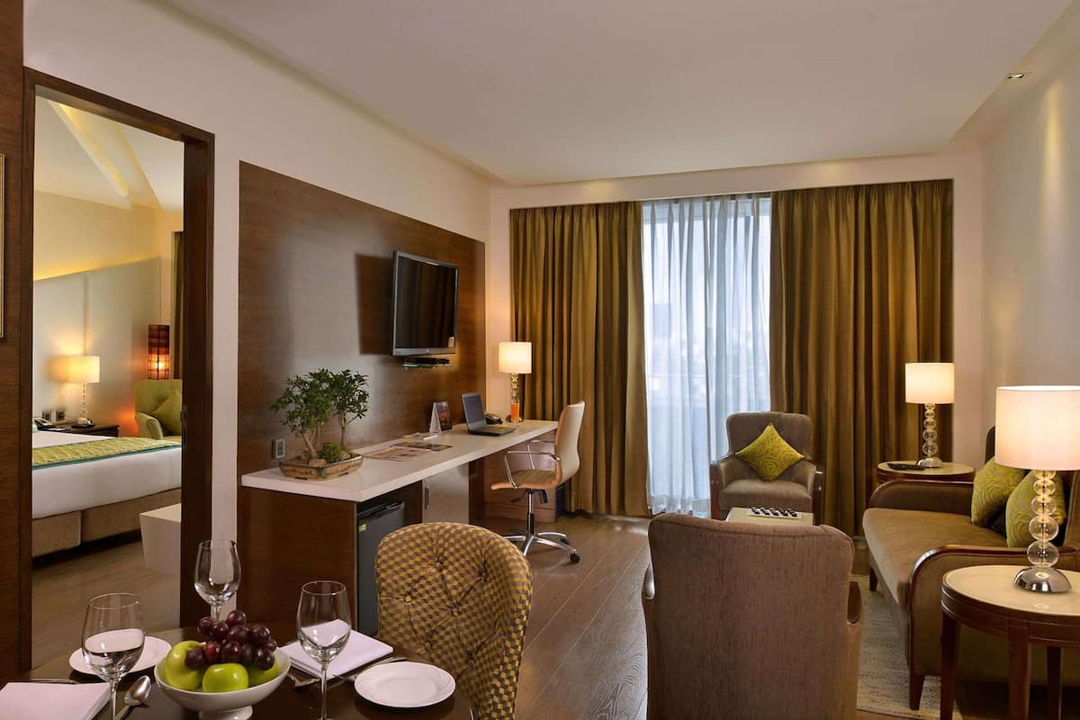 Une chambre d’hôtel comprenant un lit, un bureau avec un ordinateur, une télévision et un coin salon avec un fauteuil et un canapé.