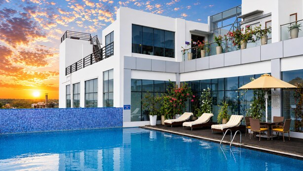 Un hôtel moderne doté d’une piscine, de chaises longues et de plantes en pot.