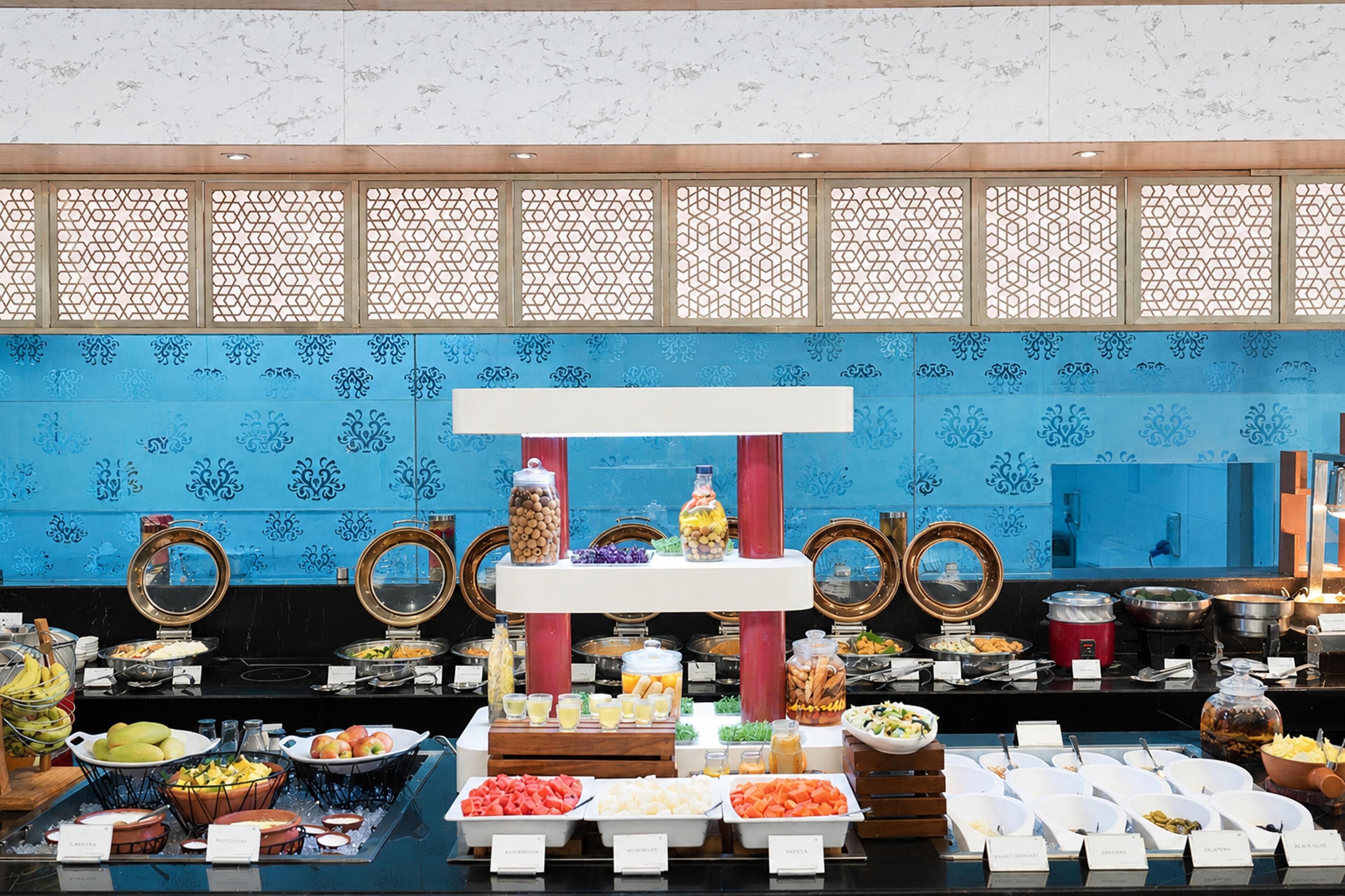 A buffet with various food items and beverages, a decorative mirror, and a blue patterned wall.