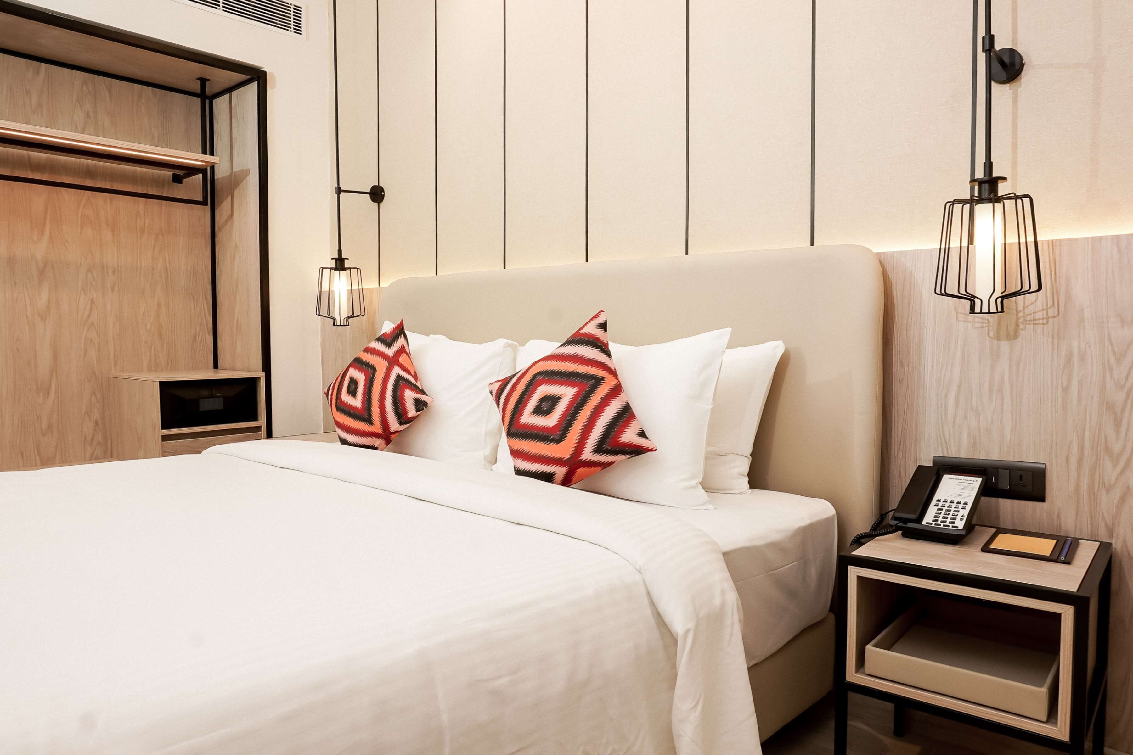 Una habitación de hotel con cama, una mesita de noche con teléfono y otra mesita de noche con lámpara.