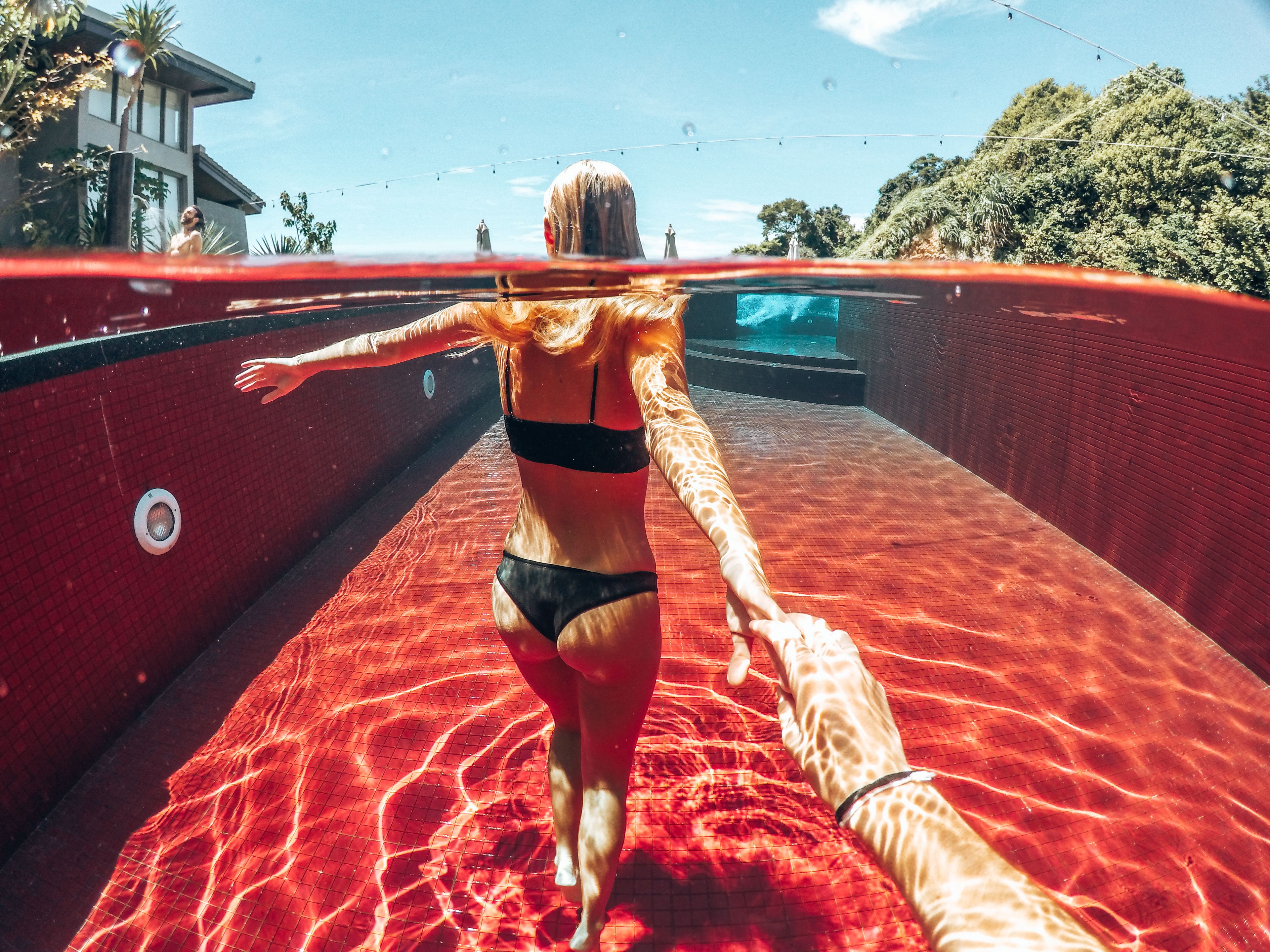 An underwater view of a swimming pool with clear water, a red tiled floor, and a person swimming.