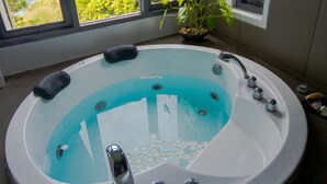 A modern bathroom with a large bathtub, a potted plant, and a view of a lush green landscape through large windows. - The Houben - Adult Only (Ko Lanta)