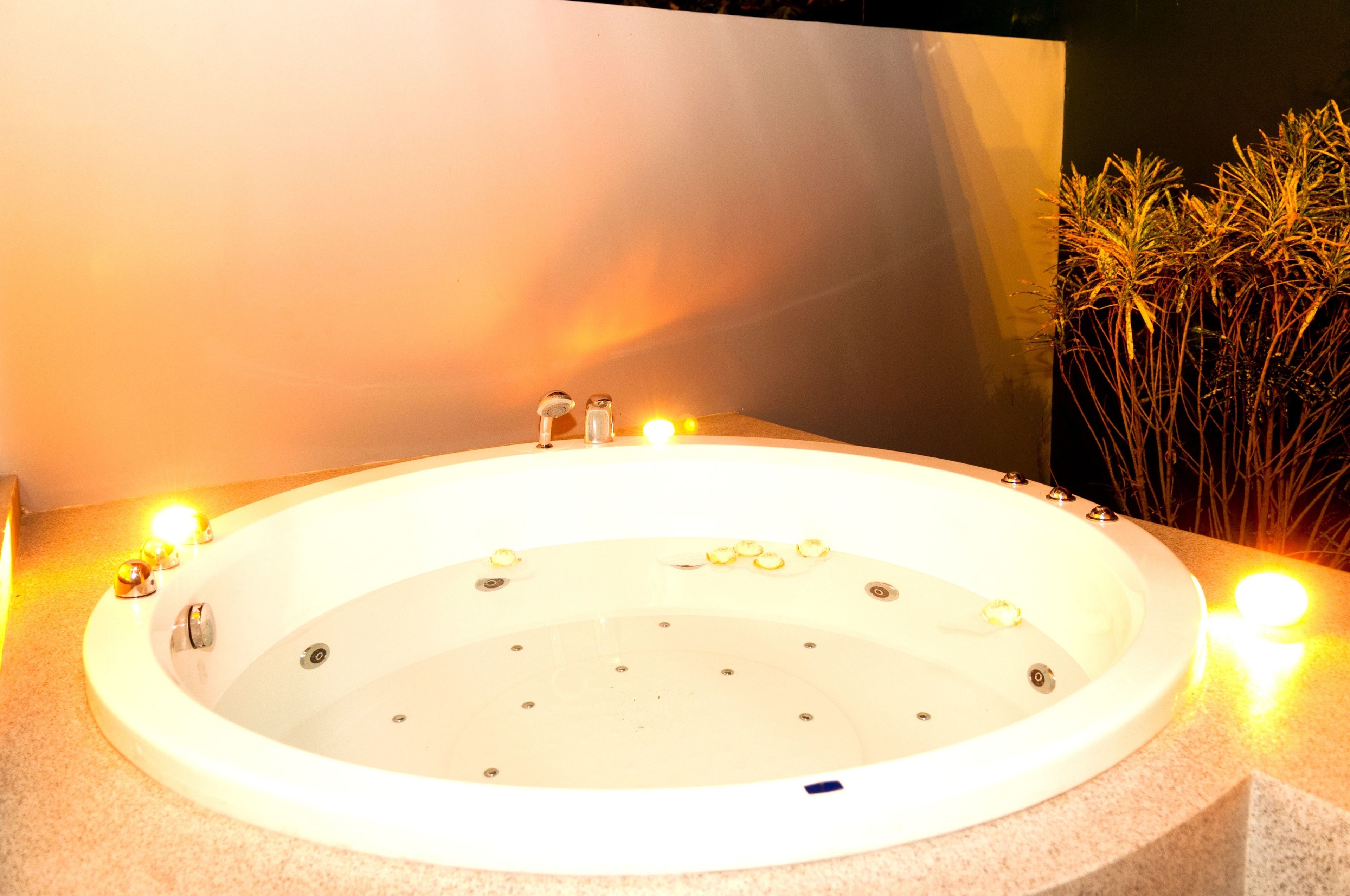 Un jacuzzi con un borde iluminado, rodeado de velas y una planta decorativa a la derecha.