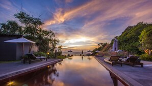 A serene pool area with lounge chairs and umbrellas, surrounded by lush greenery and a view of the ocean at sunset. - The Houben - Adult Only (Ko Lanta)
