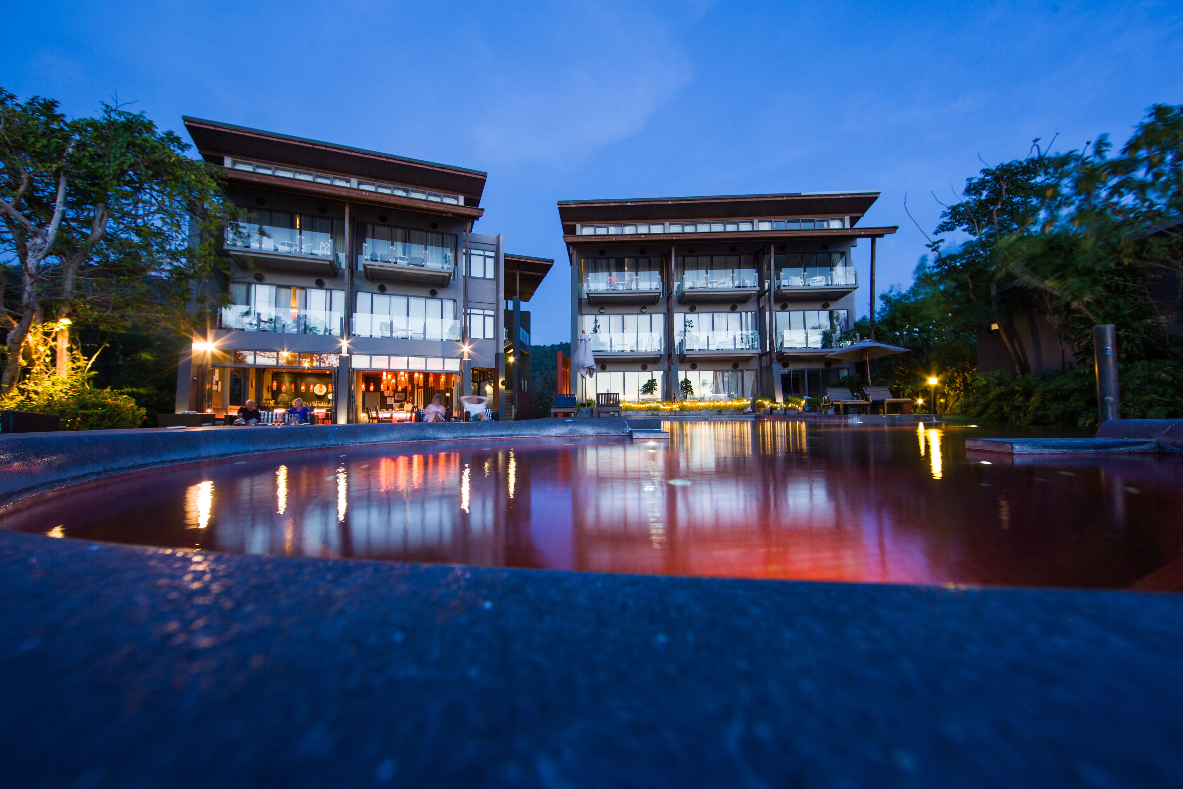 A modern hotel with a reflective pool in front, featuring a multi-story structure with balconies and large windows.