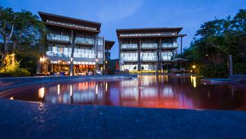 A modern hotel with a reflective pool in front, featuring a multi-story structure with balconies and large windows.