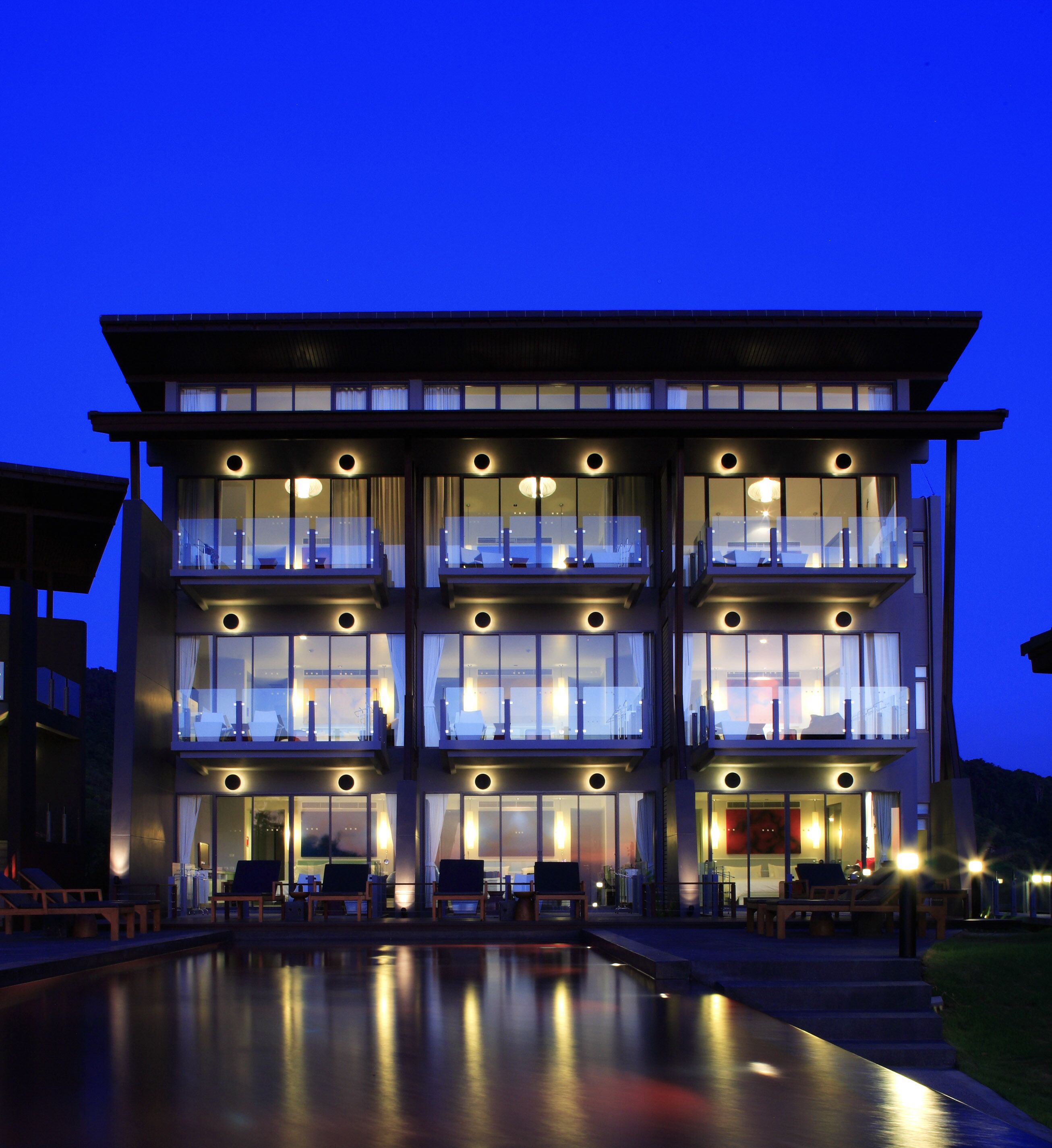 A multi-story hotel with balconies, a swimming pool, and a well-lit facade.