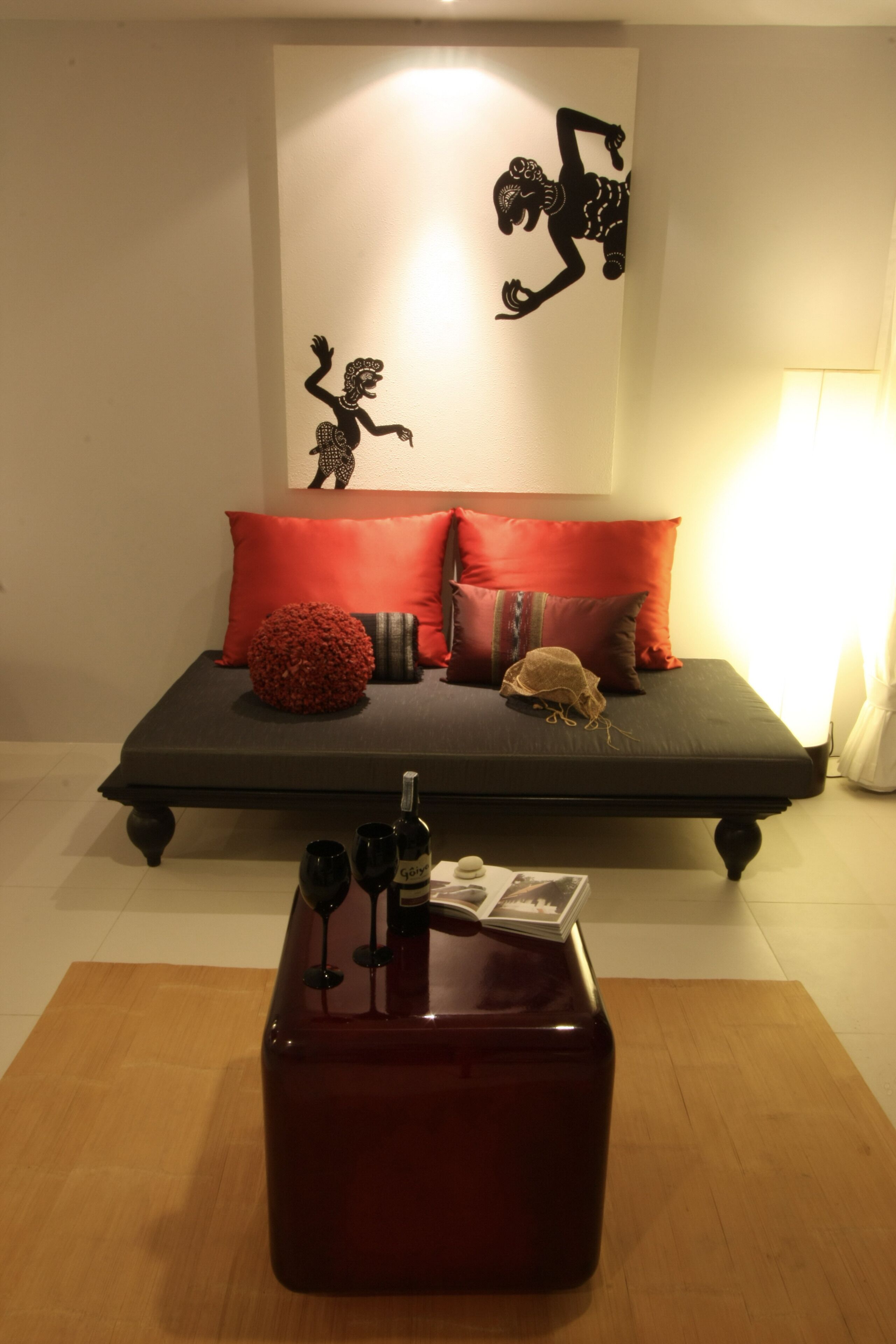A bedroom with a bed, red pillows, a decorative wall piece, and a wooden table with wine glasses.