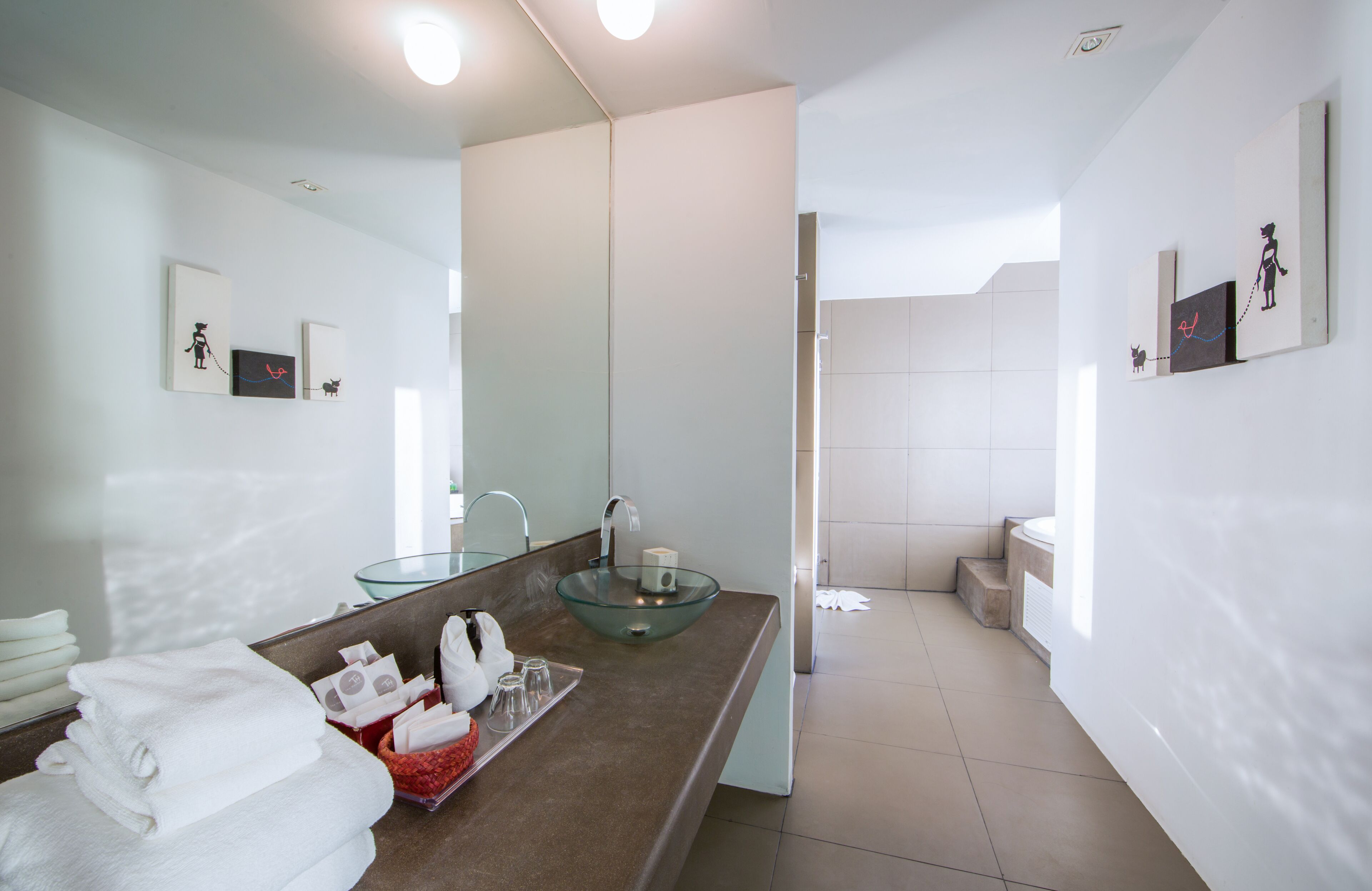 A modern bathroom with a glass sink, white towels, and artwork on the walls.