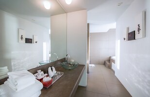 A modern bathroom with a glass sink, white towels, and artwork on the walls.